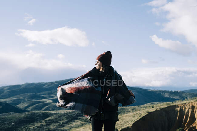 Giovane turista contemplativa femminile con tessuto guardando lontano contro la montagna verde durante il viaggio alla luce del sole — Foto stock