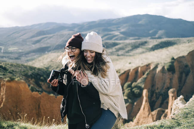 Cheerful best female friends with photo camera having fun against mount and gorge on sunny day in back lit — Stock Photo