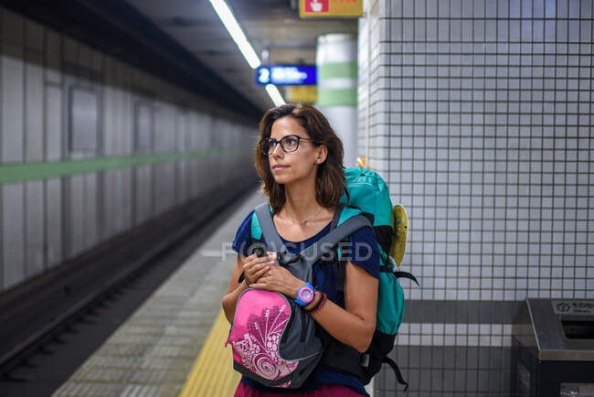 Молодая белая женщина-путешественница с рюкзаком ждет поезд на станции метро, Токио, Япония — стоковое фото