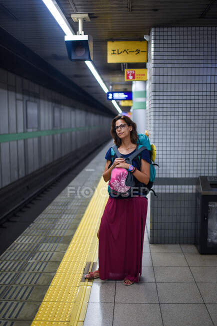 Кавказька молода жінка - мандрівниця з рюкзаком чекає поїзд на станції метро (Токіо, Японія). — стокове фото