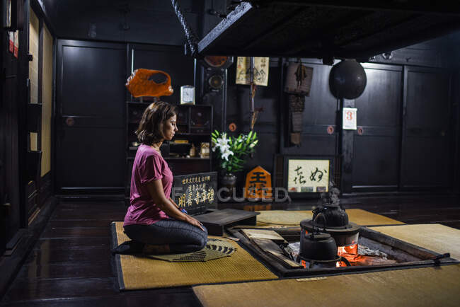 Junge kaukasische Frau kniet vor einem Feuer in einem traditionellen japanischen Haus — Stockfoto