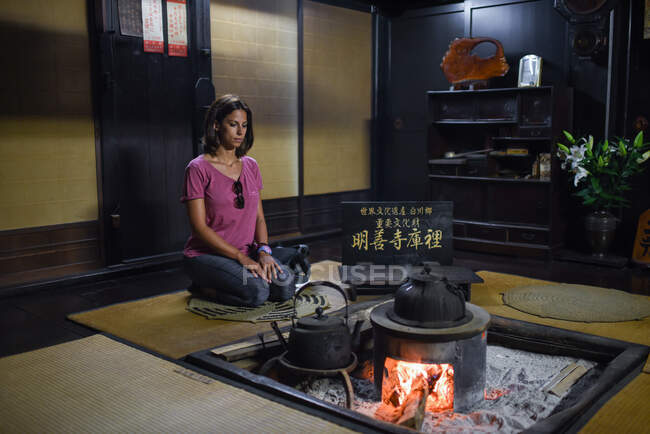 Giovane donna caucasica inginocchiata davanti a un fuoco all'interno di una casa tradizionale giapponese — Foto stock