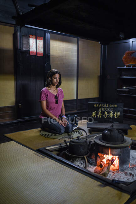 Jovem caucasiana ajoelhada em frente a um incêndio dentro de uma casa tradicional japonesa — Fotografia de Stock