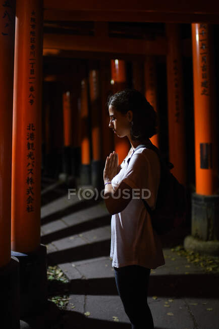Молода кавказька жінка молиться разом у святині Фусімі Інарі (Fushimi Inari Taisha) в оточенні воріт хребетних у нічний час, Кіото, Японія. — Stock Photo