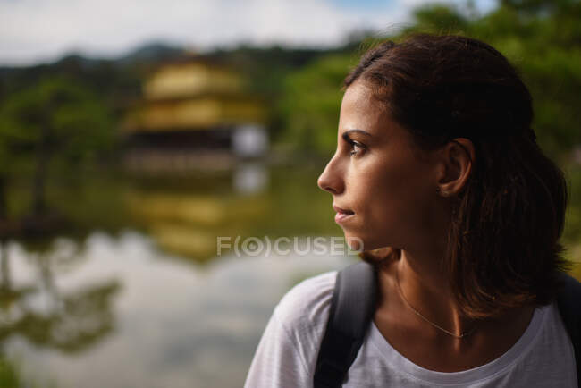 Perfil de close retrato de jovem caucasiana com Kinkaku-ji (Pavilhão Dourado) Templo Zen no fundo, Kyoto, Japão — Fotografia de Stock