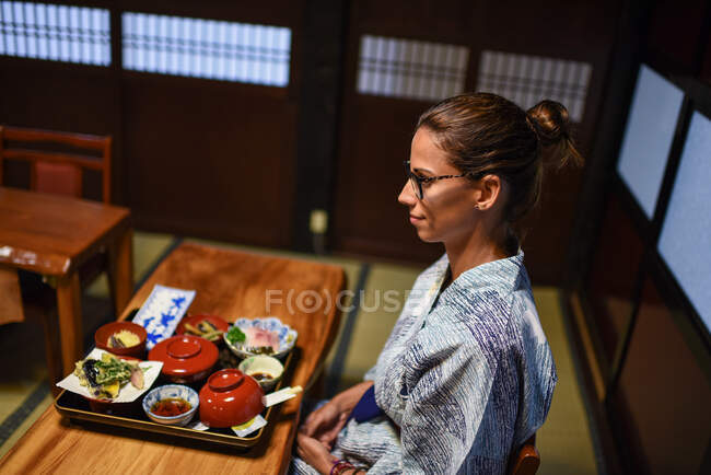 Молодая кавказка в кимоно сидит за столом в традиционном японском доме — стоковое фото