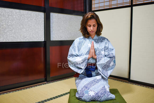 Portrait intérieur d'une jeune femme caucasienne agenouillée avec les mains en prière portant un kimono japonais traditionnel à l'intérieur d'une maison, Ainokura, Japon — Photo de stock