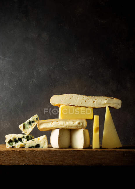 Varios quesos cortados sobre tabla de madera colocados sobre mesa de madera - foto de stock