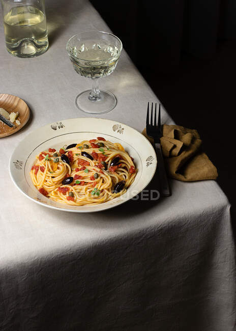 Spaghetti alla Puttanesca servidor com vidro oh vinho branco colocado na mesa com guardanapo — Fotografia de Stock