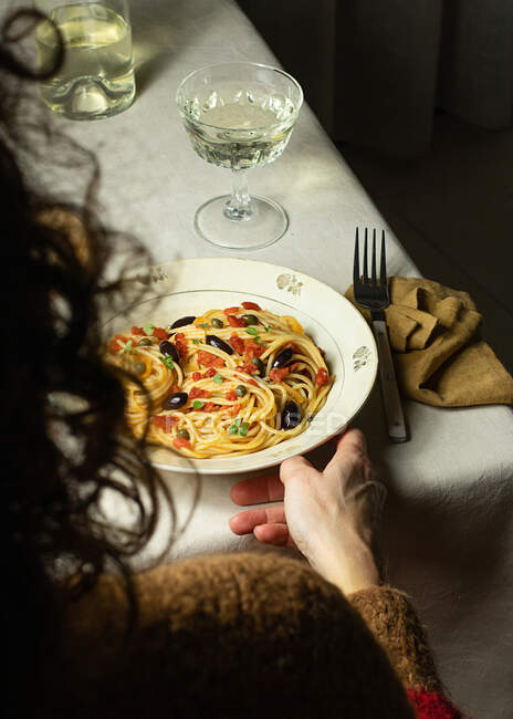 Cultivé personne méconnaissable manger Spaghetti alla Puttanesca serveur avec verre oh vin blanc placé sur la table avec serviette — Photo de stock