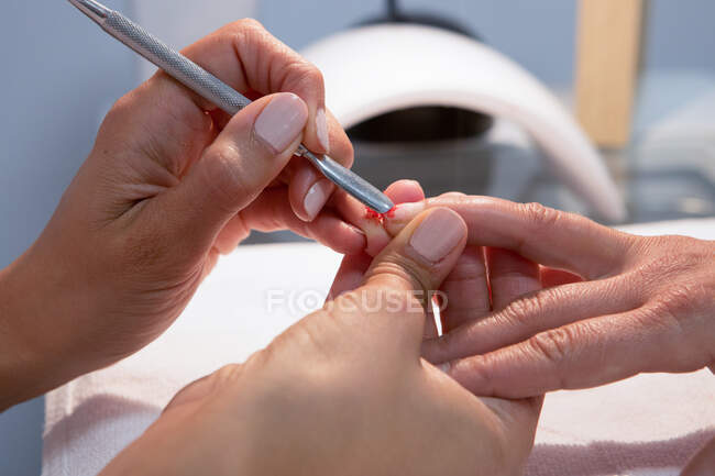 Ritagli il padrone di bellezza femminile irriconoscibile che applica la vernice rossa a unghia di donna durante procedura di manicure in centro termale — Foto stock