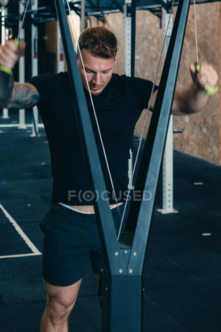 Muscular determined male athlete doing exercises on cable crossover machine during functional workout in gym — Stock Photo