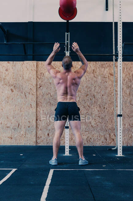 Back view of unrecognizable sportsman with naked torso throwing medicine ball during functional workout in gym — Stock Photo