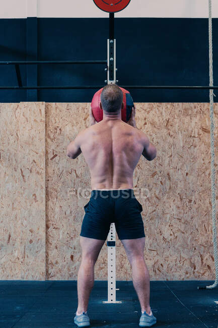 Back view of unrecognizable sportsman with naked torso throwing medicine ball during functional workout in gym — Stock Photo