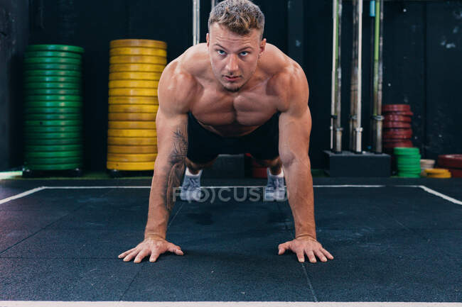 Atleta masculino focado com tronco nu muscular fazendo flexões durante o treino funcional e olhando para a frente — Fotografia de Stock