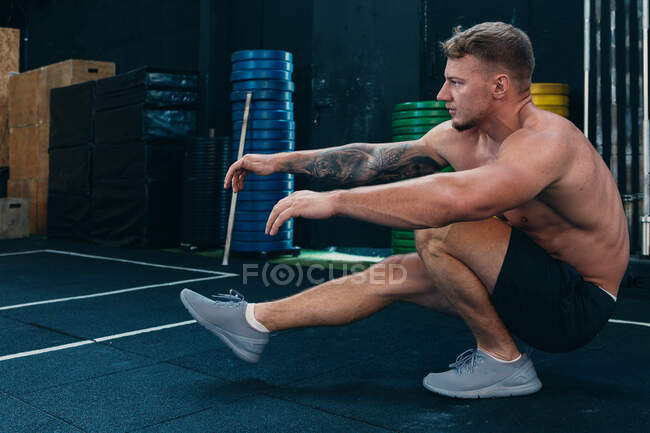 Vista lateral do atleta masculino sem camisa fazendo agachamentos de pistola durante o treinamento funcional no ginásio — Fotografia de Stock