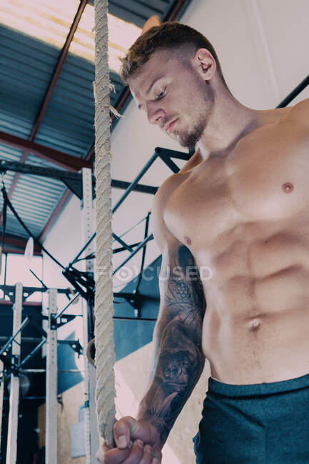 Niedriger Winkel des muskulösen männlichen Athleten mit nacktem Oberkörper, der sich während des Functional Trainings auf Übungen mit dem Seil in der Turnhalle vorbereitet — Stockfoto