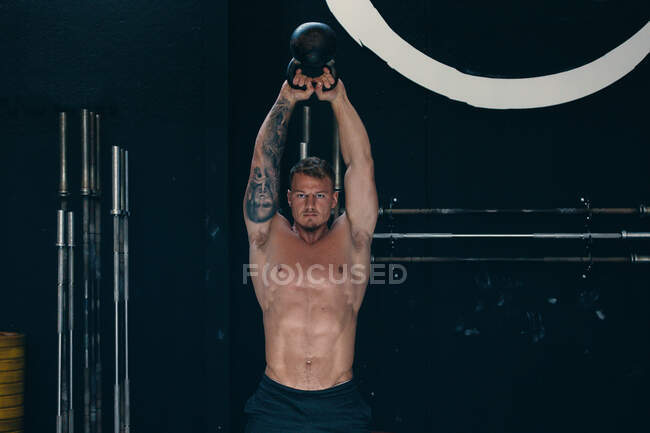 Atleta masculino determinado com tronco nu fazendo kettlebell arrebatar exercício durante o treino funcional no ginásio — Fotografia de Stock