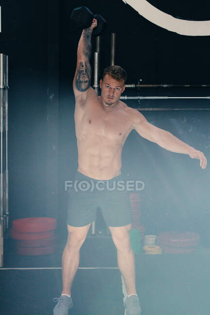 Athlète masculin déterminé avec torse nu faisant kettlebell arracher exercice pendant l'entraînement fonctionnel dans la salle de gym — Photo de stock