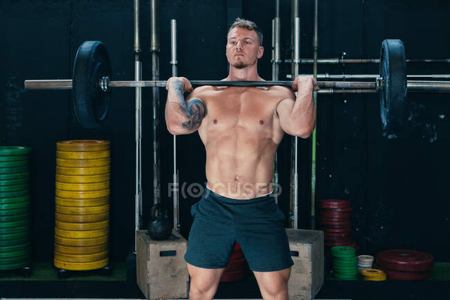 Athlète masculin fort faisant haltérophilie avec haltère lourde pendant l'entraînement dans la salle de gym — Photo de stock