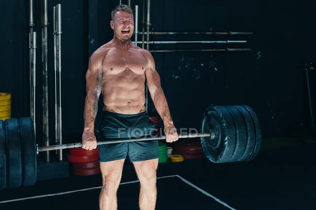 Atleta masculino forte fazendo deadlift com barra pesada enquanto gritava durante o treino no ginásio — Fotografia de Stock