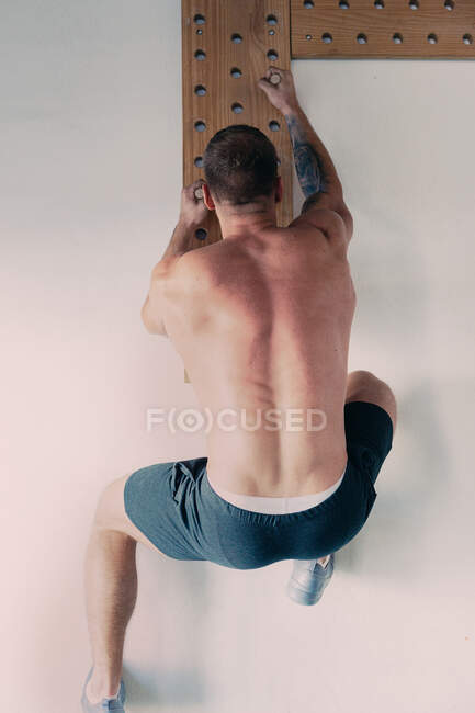 Vue arrière du pegboard masculin d'escalade d'athlète musculaire méconnaissable pendant l'entraînement fonctionnel dans la salle de gym — Photo de stock