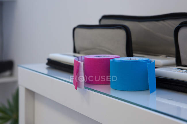 Cintas Kinesio rosa y azul con superficie elástica cerca del equipo médico en casos de escritorio en la habitación - foto de stock