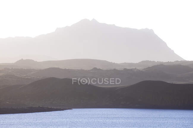 Scenic view of spacious hilly terrain covered with grass near calm vast lake on peaceful foggy morning — Stock Photo