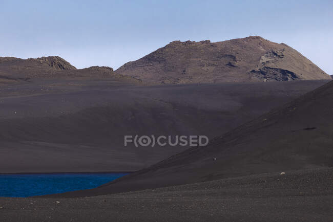 Pintoresca vista de las ásperas tierras altas rocosas en el valle estéril con un pequeño estanque tranquilo bajo el cielo azul sin nubes - foto de stock