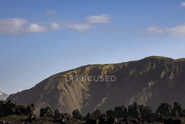 Vue panoramique de formations volcaniques rocheuses rugueuses entourées de montagnes sèches vallonnées — Photo de stock