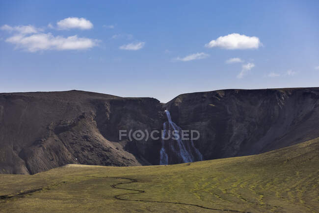 Erstaunliche Landschaft von grünem, hügeligem Gelände mit rasanter Kaskade, die von felsigen, rauen Gebirgszügen abfließt — Stockfoto