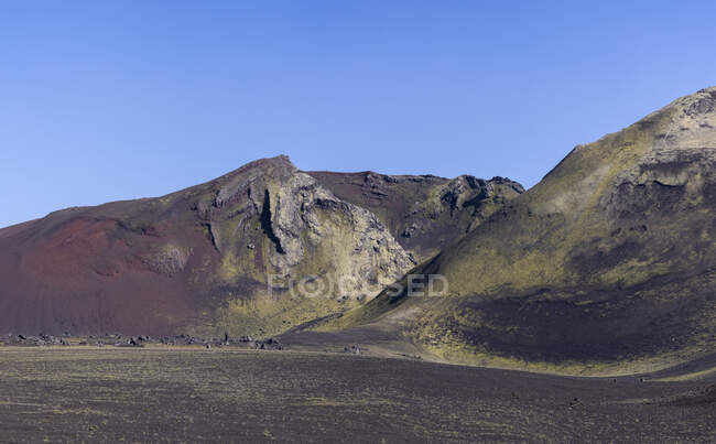 Paysage spectaculaire d'un terrain rocheux accidenté sans fin avec des pentes sèches et une végétation aléatoire située sous un ciel bleu clair en Islande — Photo de stock