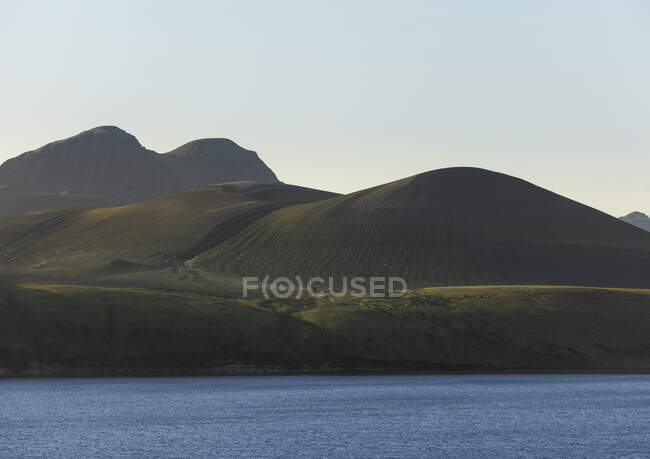 Wonderful scenery of cold crystal clear lake surrounded by rough mountain range covered with dry vegetation on clear day — Stock Photo