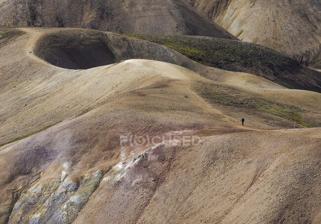 Неузнаваемый турист в повседневной одежде прогуливается по сухой вершине холма против живописной горной местности в солнечный день — стоковое фото