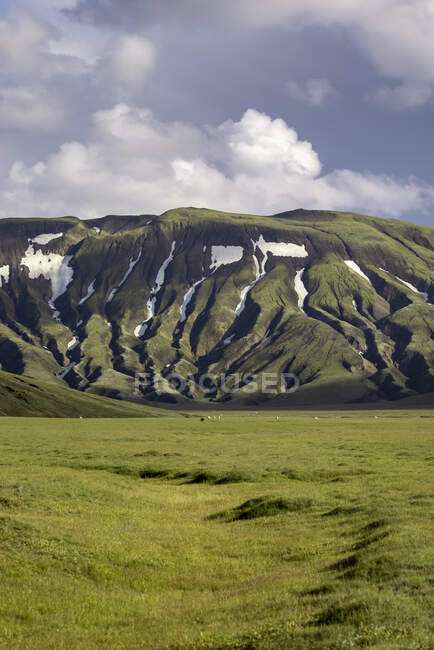Paesaggio pittoresco di ruvida catena montuosa verde con neve sul pendio situato su un lussureggiante prato erboso — Foto stock