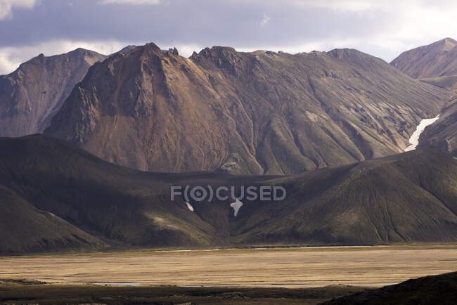 Paisagem incrível de montanha dramática rochosa perto de colinas verdes e lago tranquilo em terras altas selvagens na Islândia — Fotografia de Stock