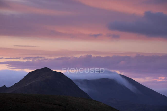 Panorama mozzafiato della catena montuosa rocciosa con cime nella densa nebbia sotto il maestoso cielo rosa al tramonto — Foto stock