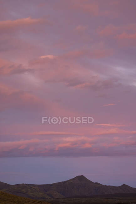Impresionante paisaje de cordillera rocosa con picos bajo majestuoso cielo rosa al atardecer - foto de stock