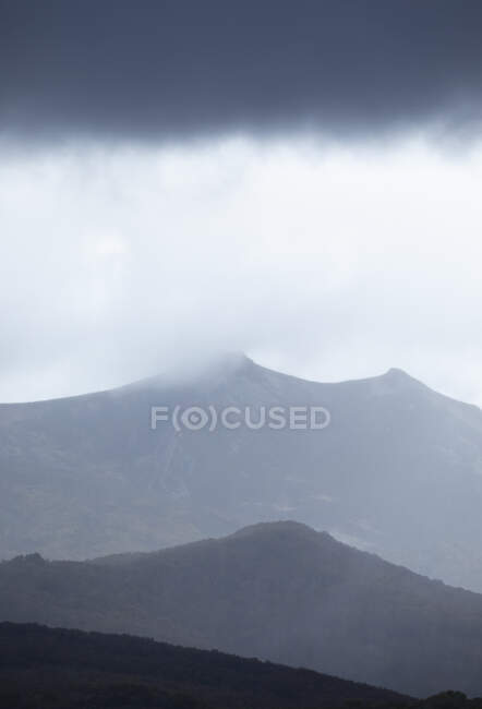 Picturesque scenery of rough mountain range with peaks in dense fog under cloudy gloomy sky in highlands — Stock Photo