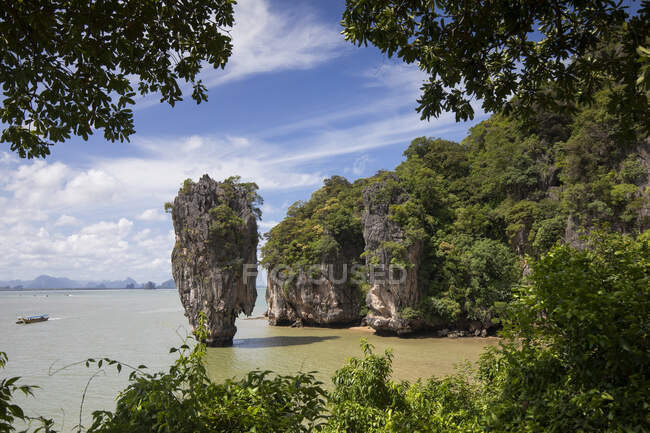 Pintoresca vista del acantilado empinado rocoso y la roca cubierta con bosque tropical bañado por el agua de mar tranquila bajo el cielo azul claro en Phuket Tailandia - foto de stock