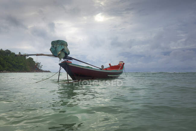 Paisaje pacífico de barco pequeño amarrado en ondulante agua de mar azul bajo el cielo nublado sombrío en el país tropical - foto de stock