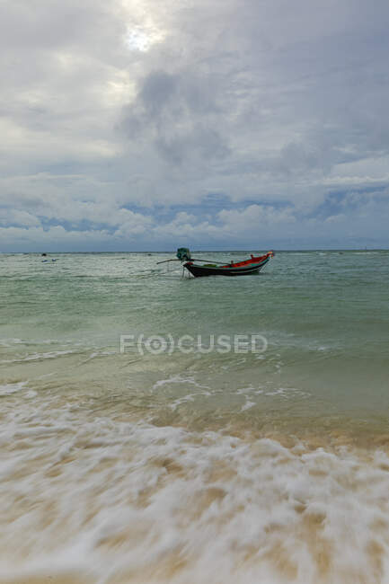 Friedliche Landschaft von kleinen Boot auf plätscherndem azurblauem Meerwasser unter bewölkten düsteren Himmel in tropischen Land vertäut — Stockfoto