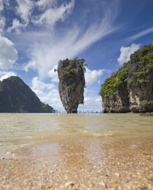 Pintoresca vista del acantilado empinado rocoso y la roca cubierta con bosque tropical bañado por el agua de mar tranquila bajo el cielo azul claro en Phuket Tailandia - foto de stock