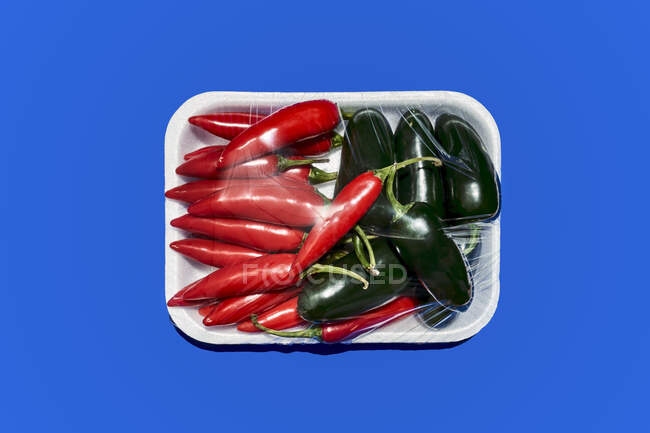 Top view of ripe chili and green spicy pepper in plastic wrap prepared for consumption on blue background — Stock Photo