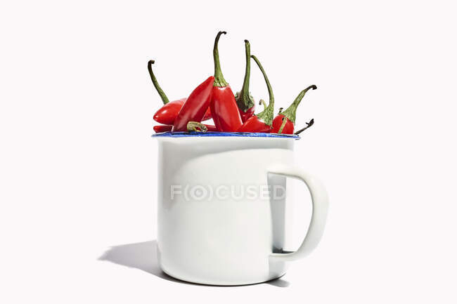Big ceramic mug full of ripe fresh exotic pepper placed on white background — Stock Photo