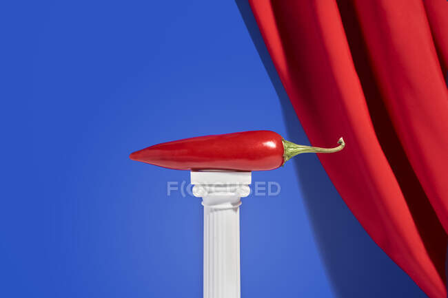 Rote Paprika auf Miniatursäule vor blauem Hintergrund mit rotem Samtvorhang — Stockfoto