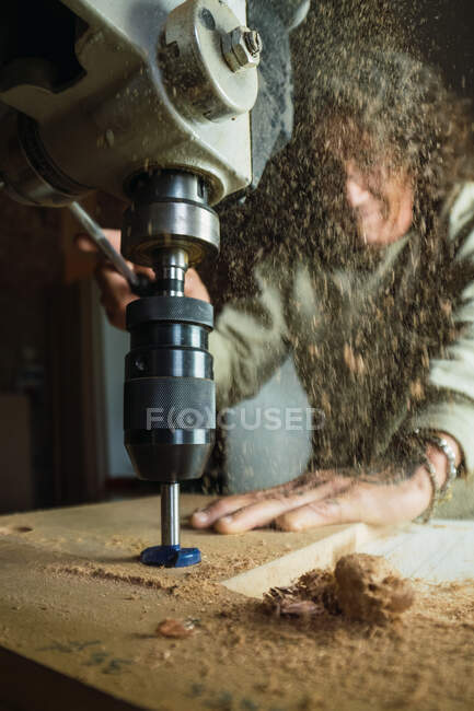 Angle bas du menuisier mâle sans trou de perçage du pouce dans la planche de bois tout en travaillant dans un atelier de menuiserie poussiéreux — Photo de stock