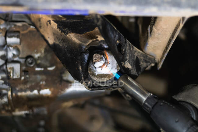 Back view of unrecognizable male auto mechanic torch while removing stripped lug nuts from car during repairing process in garage — Stock Photo