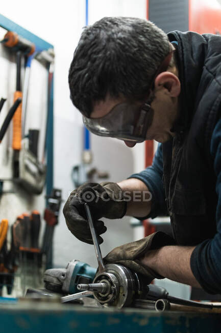 Vista lateral del mecánico auto adulto concentrado en gafas protectoras y guantes montando el cojinete del cigüeñal mientras trabaja en el garaje - foto de stock