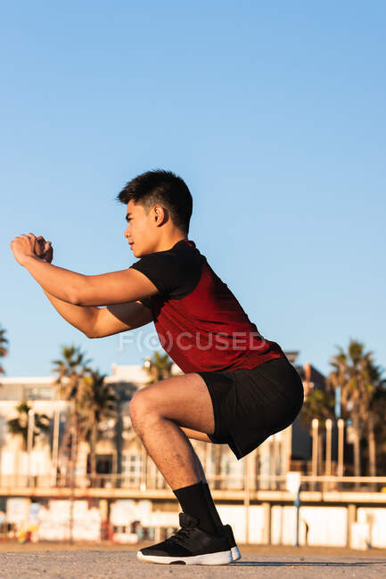 Vue latérale complète du corps d'un jeune homme asiatique déterminé dans des équipes performantes de vêtements de sport tout en se réchauffant et en se préparant sur un terrain de sport — Photo de stock
